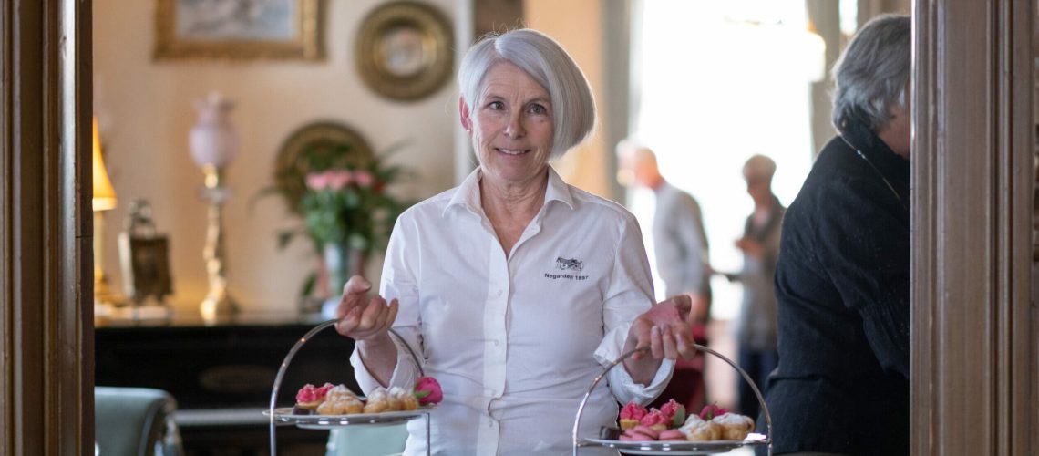 bildet viser en dame med hvit bluse som holder to afternoon tea fat